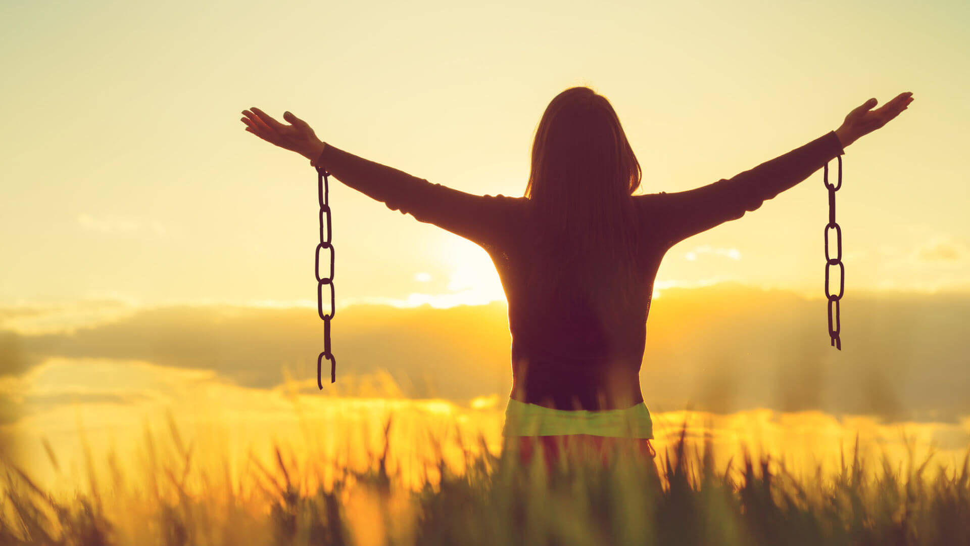 Image of a girl looking at the sunrise with broken chains hanging off her wrists.